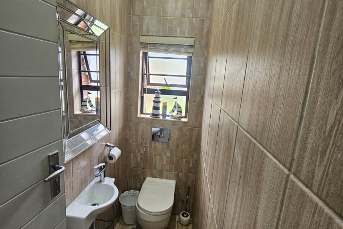 A compact guest bathroom featuring floor-to-ceiling wood-look tiling, a wall-mounted toilet, and a small corner basin.