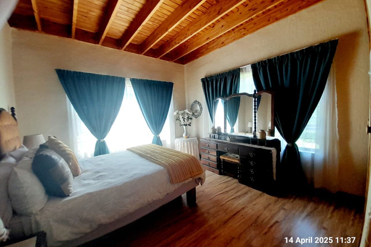 A bedroom featuring exposed timber beam ceilings and wood-look flooring, providing a rustic aesthetic with ample natural light from large windows.