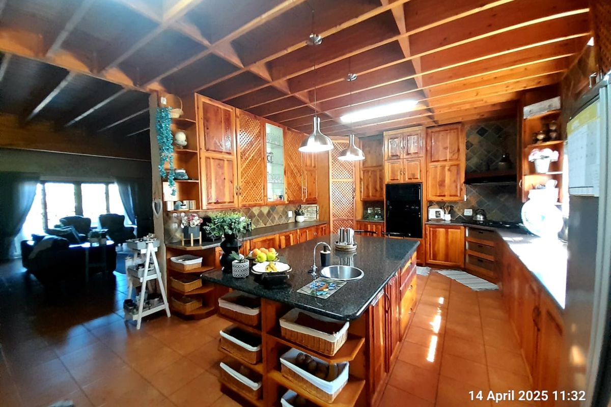 Spacious farmhouse kitchen featuring extensive timber cabinetry, a central island with granite countertop, and exposed wooden beam ceilings.