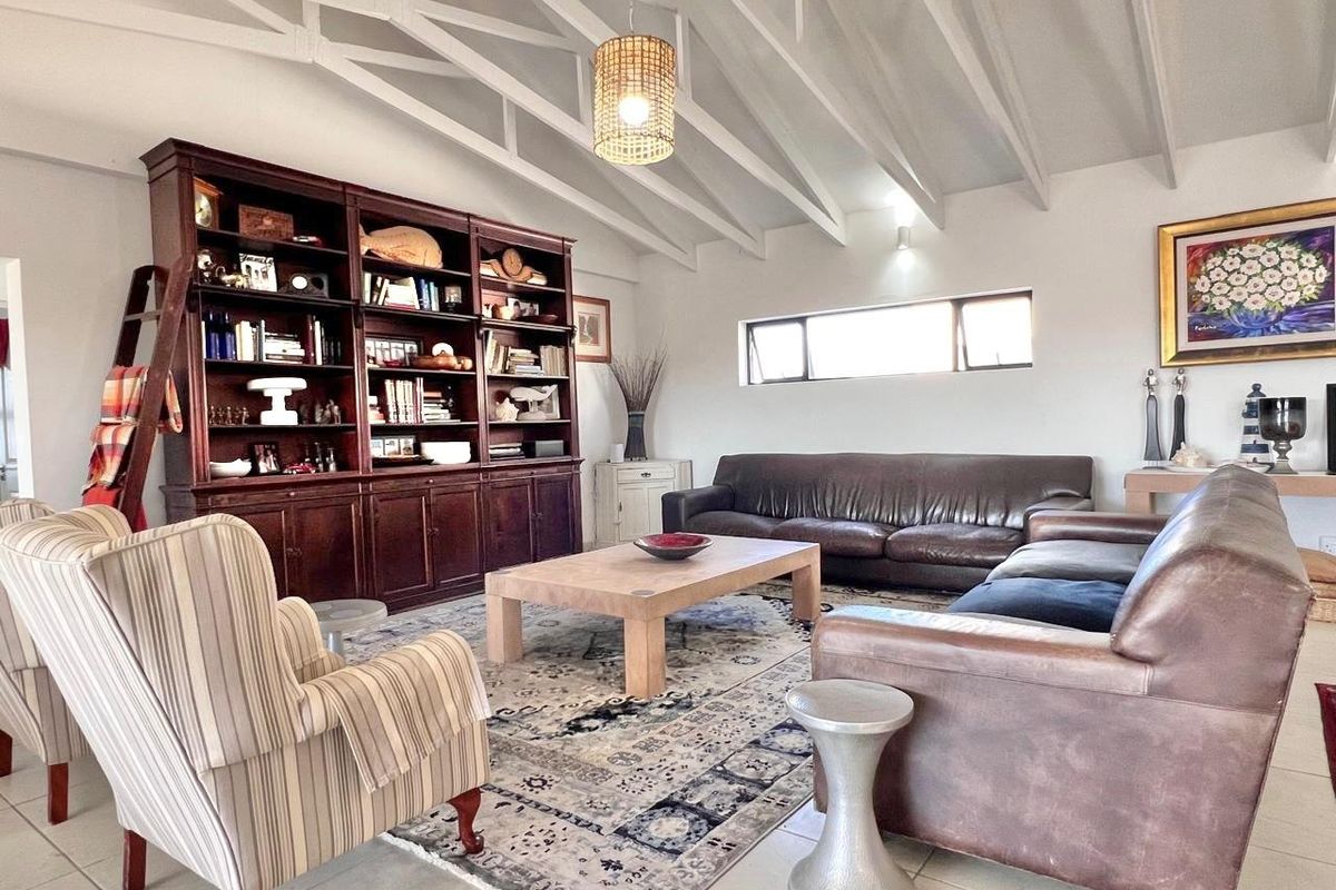 Spacious living room featuring high vaulted ceilings with exposed beams, tiled flooring, and a large built-in wooden bookshelf unit.