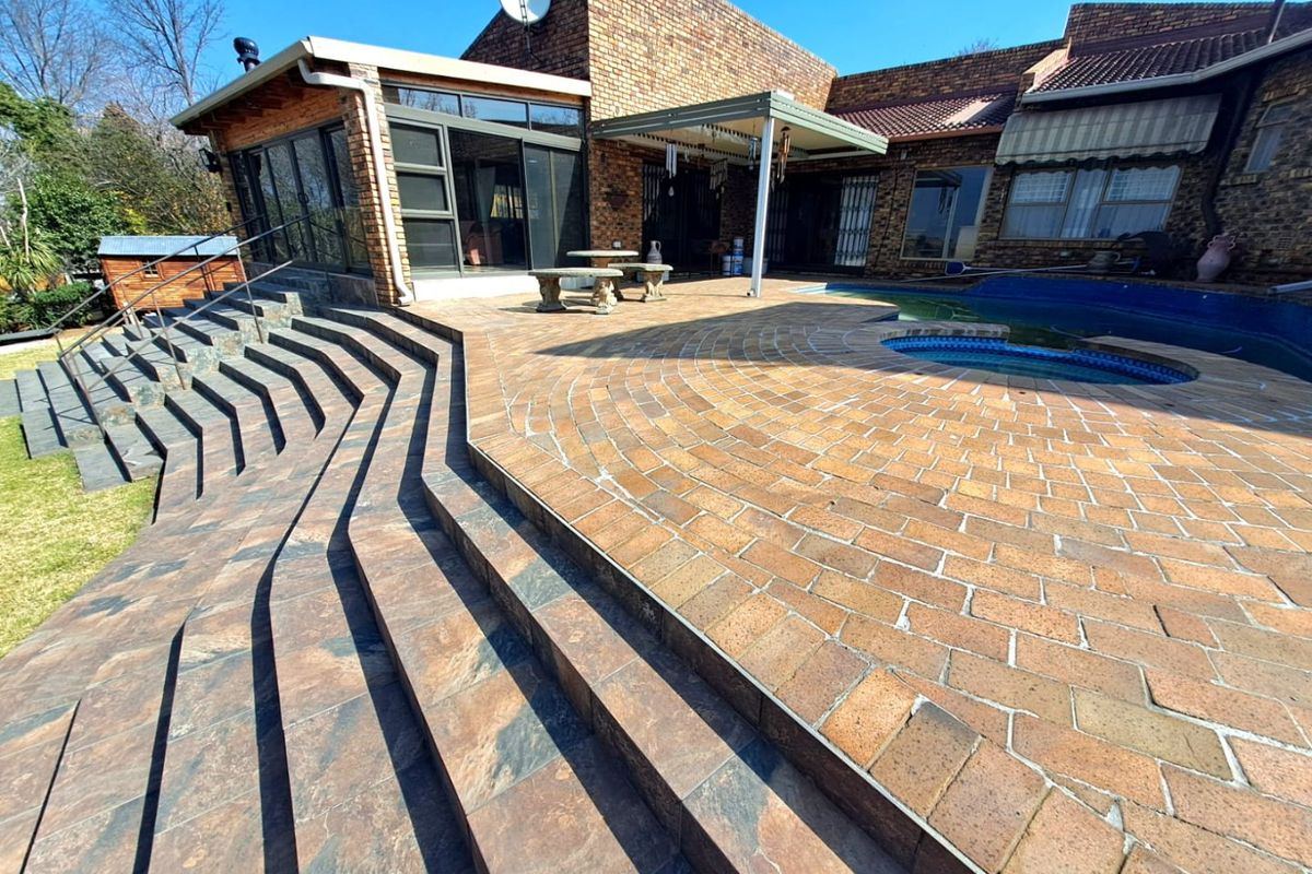 Spacious rear patio area featuring tiered slate stairs, brick paving, and an integrated swimming pool with a built-in spa section.