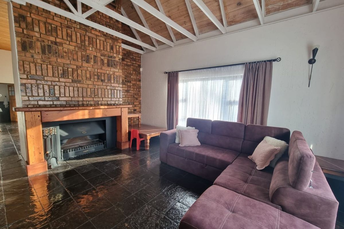 Spacious living room featuring a prominent exposed brick fireplace, vaulted timber-beamed ceiling, and dark tiled flooring.