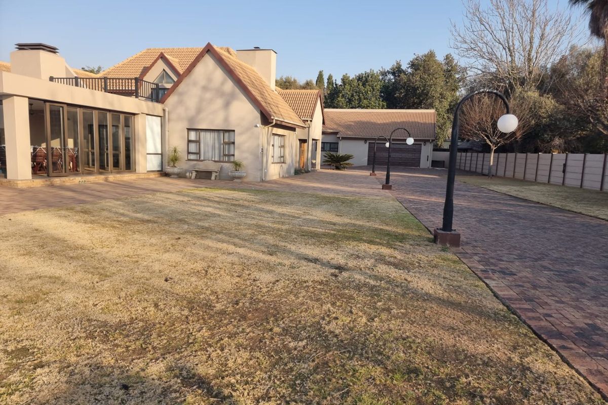 Spacious exterior view of the property featuring a paved driveway, large lawn area, and a multi-section house with a garage and patio.