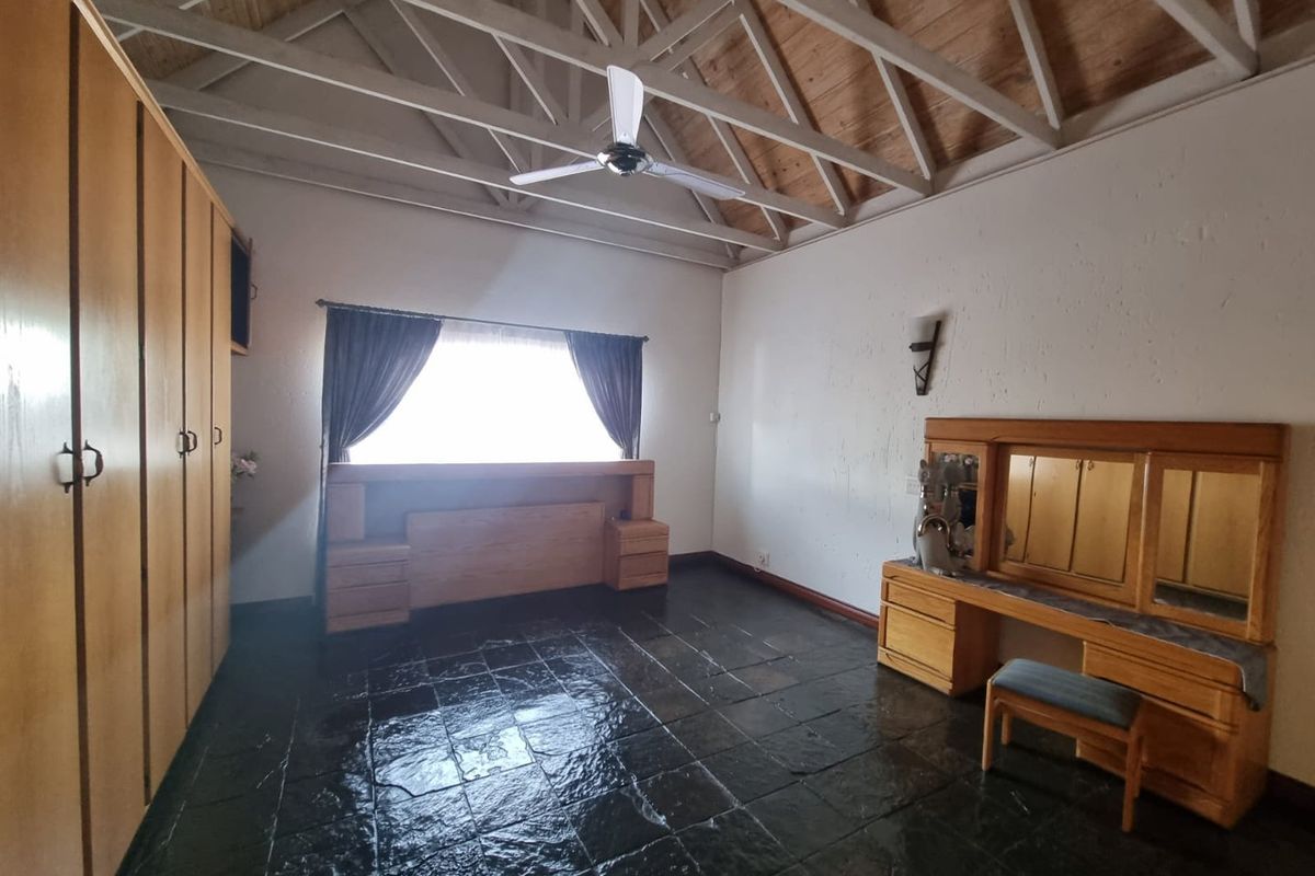 Spacious bedroom featuring high vaulted timber ceilings, exposed trusses, built-in wooden cabinetry, and dark slate flooring.