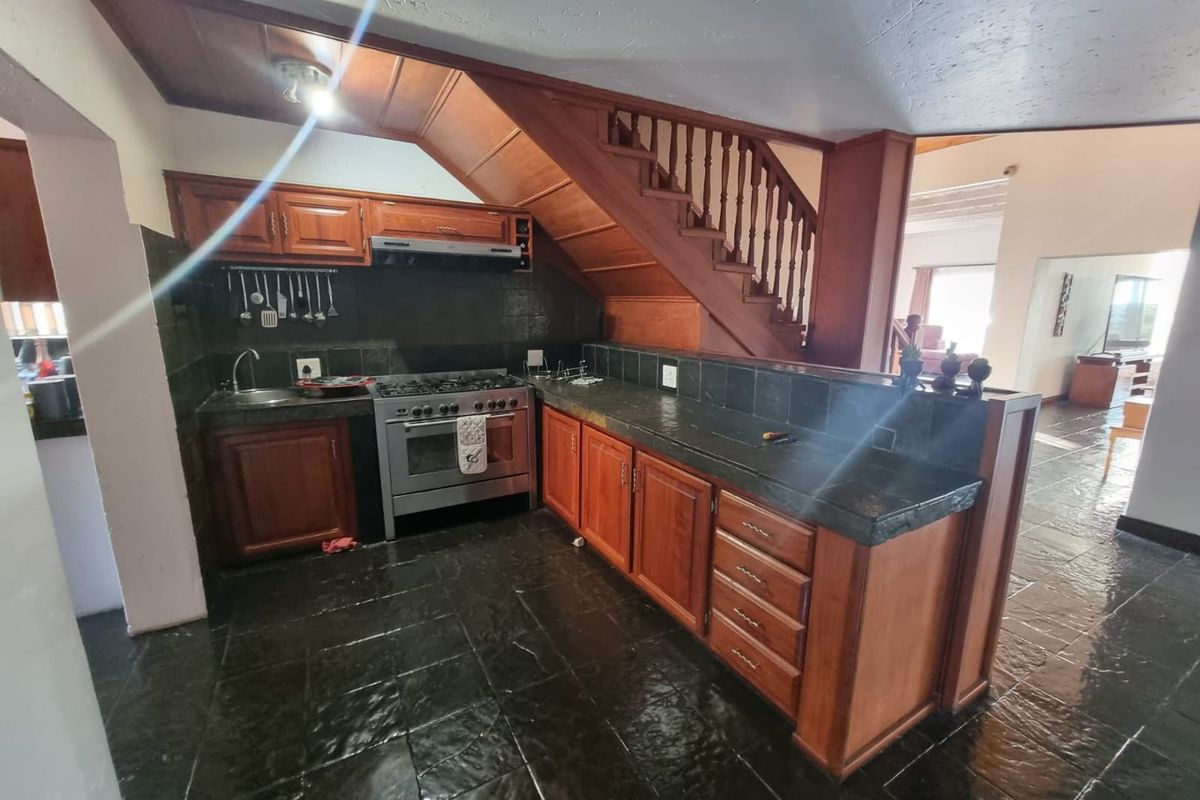 A kitchen featuring wooden cabinetry, dark stone-look tiled countertops, a gas stove with extractor fan, and integrated staircase access.