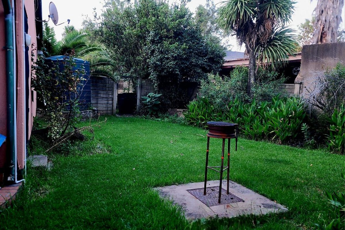 A private rear garden featuring a lawn area, established trees, perimeter boundary walls, and a dedicated concrete base for outdoor cooking.