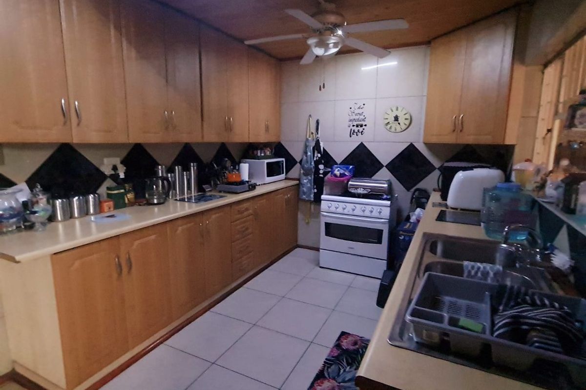 A functional kitchen featuring wood-finish cabinetry, tiled splashbacks, a built-in stove, and a double-basin sink with tiled flooring.