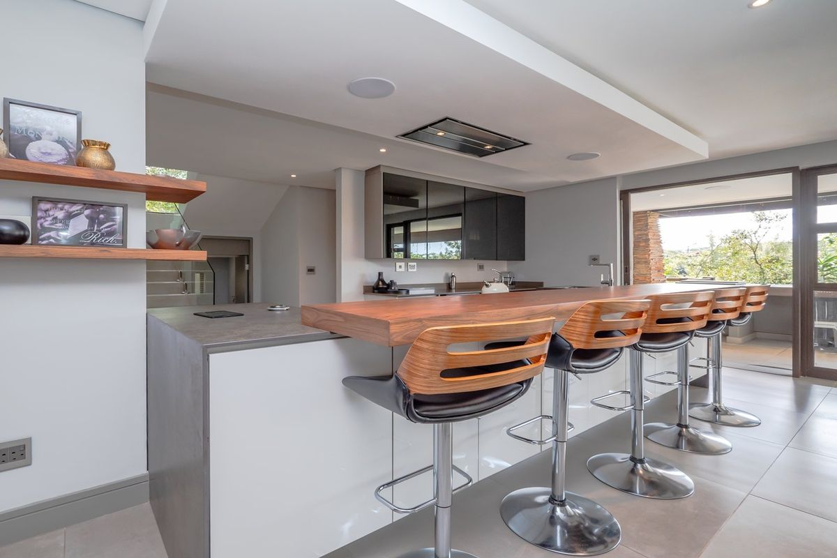 Modern kitchen featuring a large island with a timber breakfast bar, sleek cabinetry, recessed lighting, and seamless access to an outdoor patio area.
