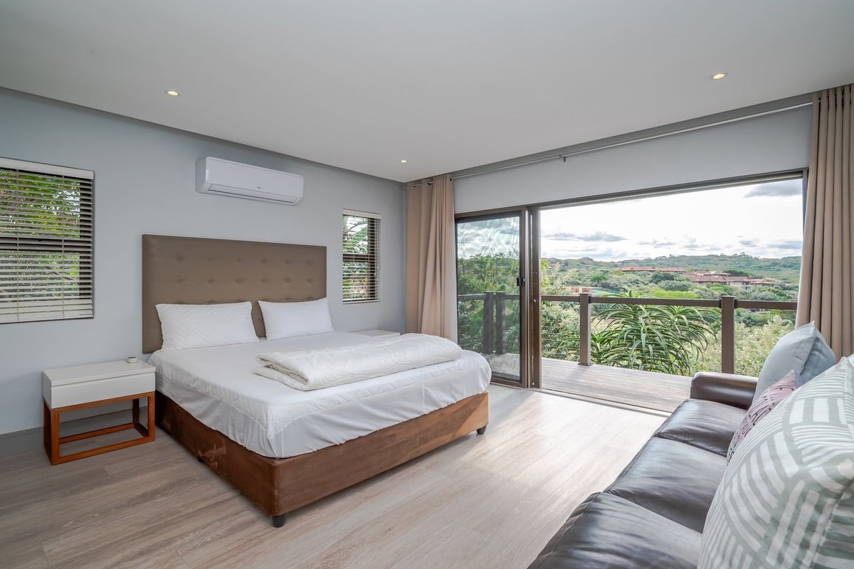 Spacious bedroom featuring light timber-look flooring, split-system air conditioning, and large sliding glass doors opening onto a private balcony with scenic views.