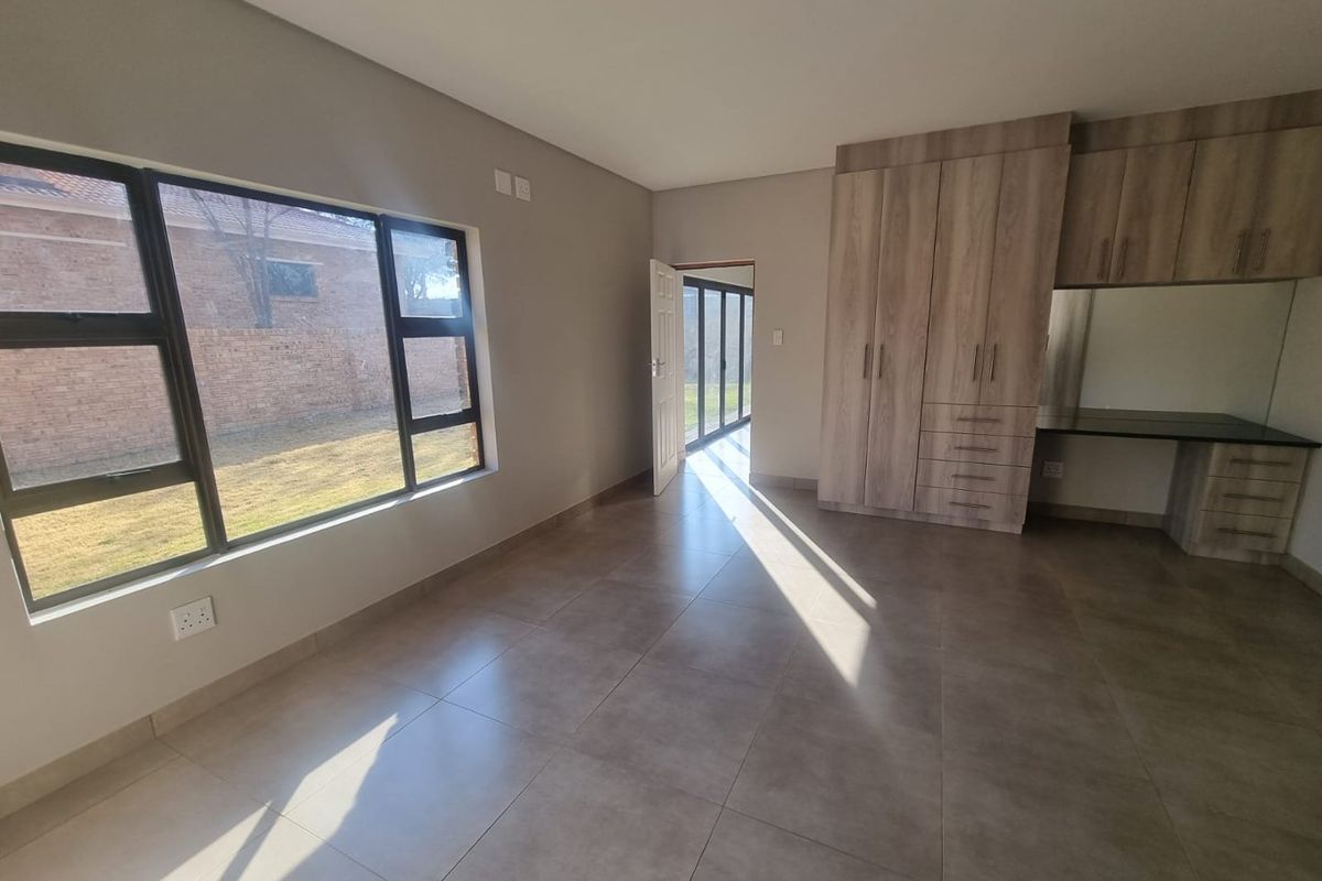 A bright, empty bedroom featuring large windows, tiled flooring, and built-in wooden cabinetry with an integrated desk area.