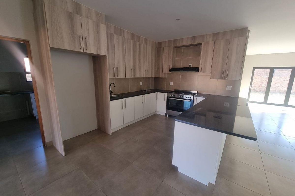 Modern open-plan kitchen featuring light wood cabinetry, dark granite countertops, a breakfast island, and a built-in oven with an extractor fan.