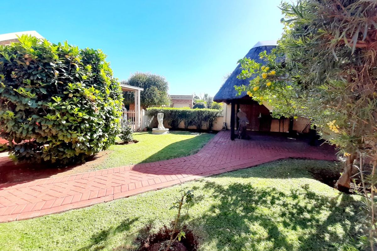 A well-maintained rear garden featuring a brick-paved pathway, lush lawn, and a traditional thatched-roof lapa area for outdoor relaxation.