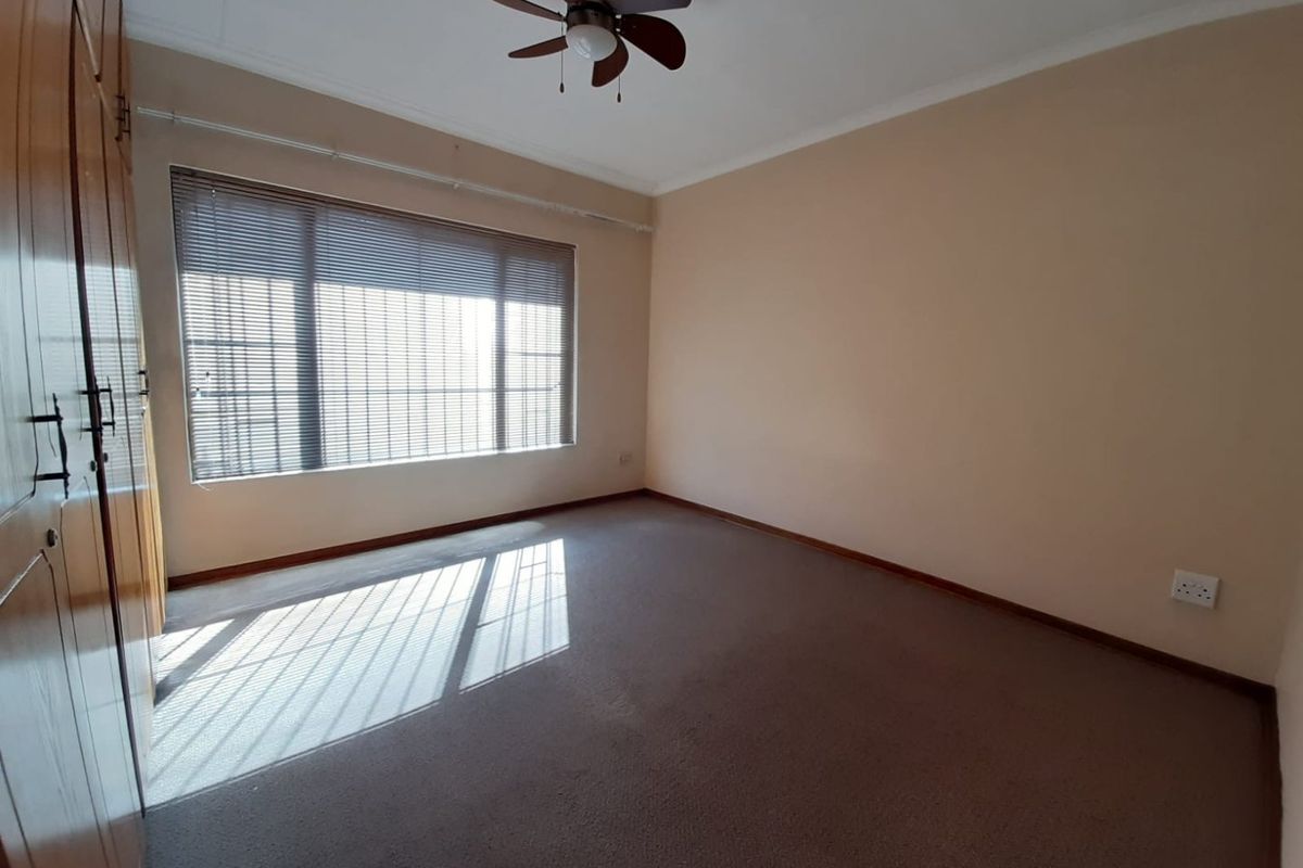 A spacious, empty bedroom featuring neutral walls, carpeted flooring, a ceiling fan, and built-in wooden wardrobes.