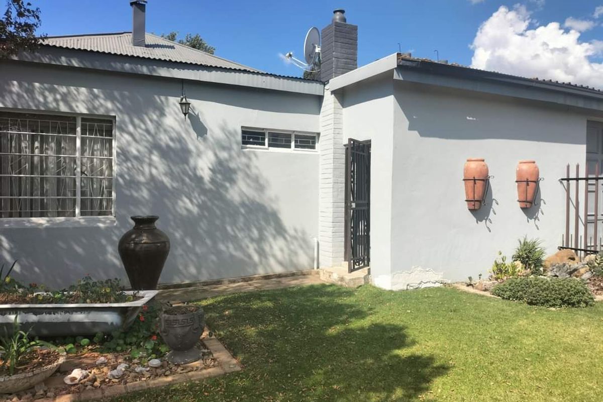 Rear exterior view of the house featuring a lawn, garden beds, security gate, and chimney stack.