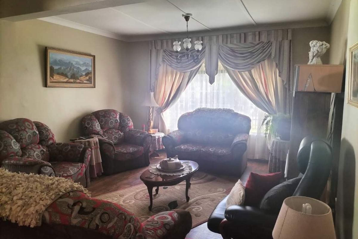 A traditional living room featuring a central chandelier, coved ceiling, and large window with draped curtains, providing a comfortable and classic living space.