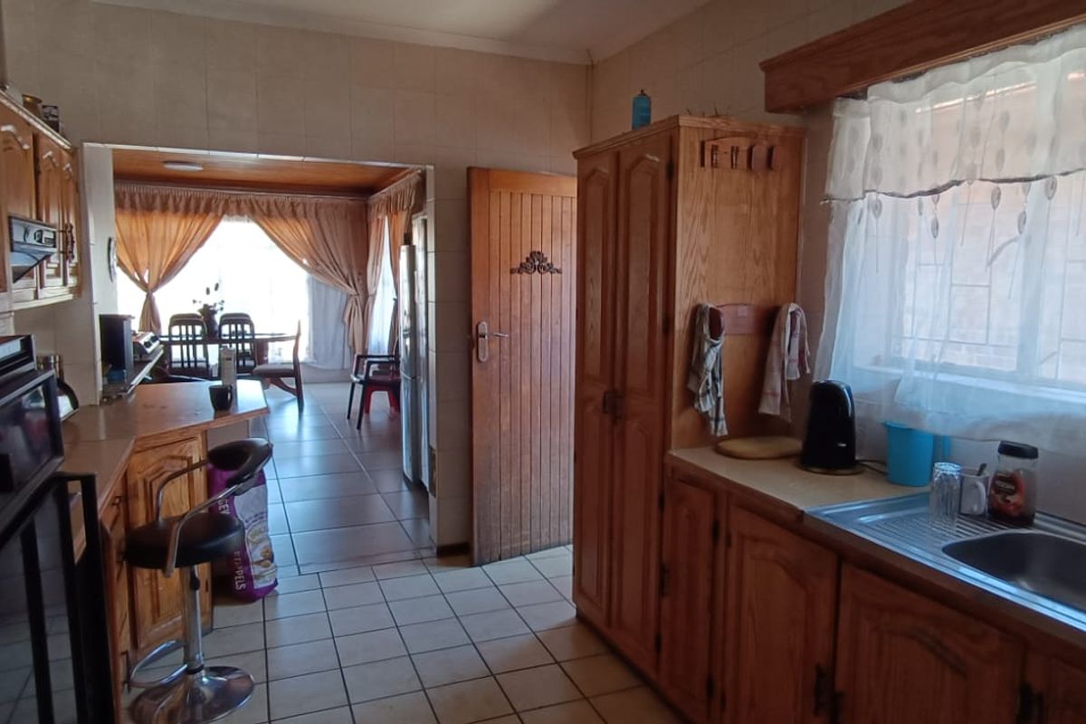 A functional kitchen featuring traditional timber cabinetry, tiled flooring, and a double sink, with an open-plan flow leading into the adjacent dining area.