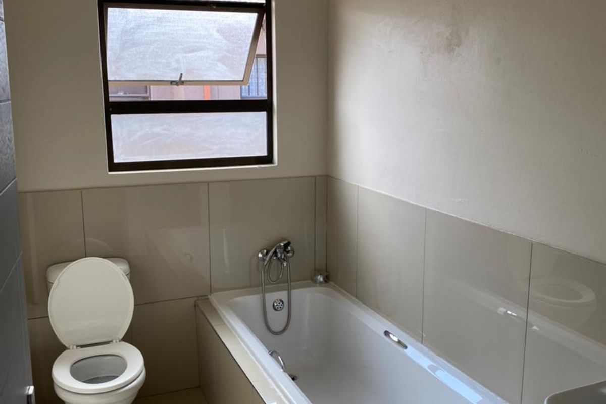 A functional bathroom featuring a built-in bathtub with shower mixer, a standard toilet, and tiled flooring with matching wall tiles.