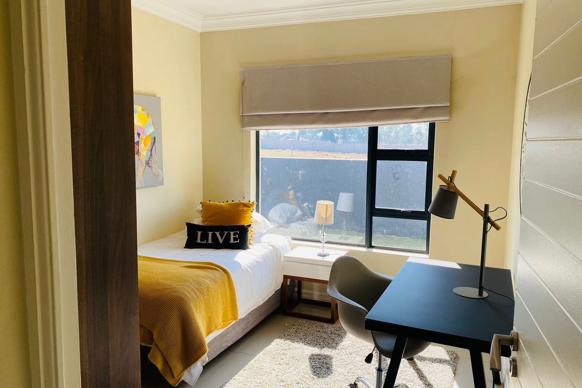 A compact bedroom featuring tiled flooring, a large window with a fitted roller blind, and recessed ceiling lighting.