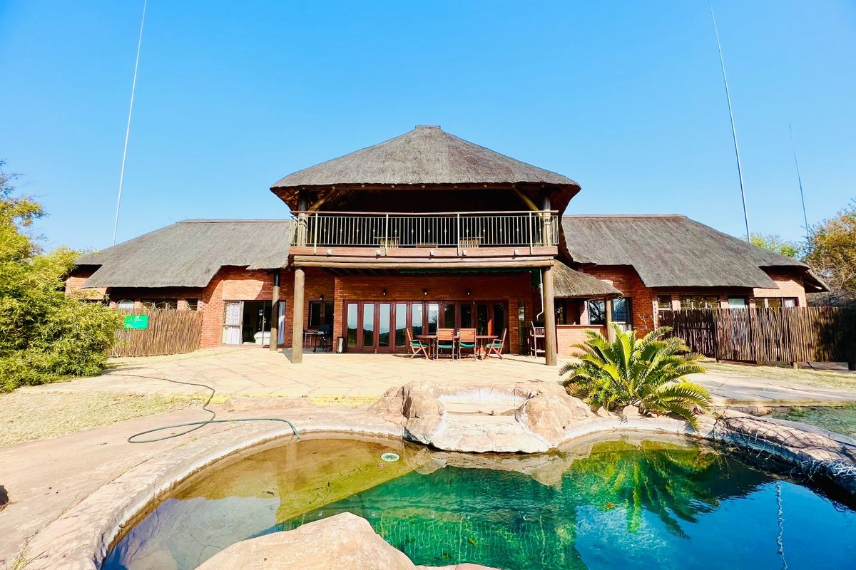 Rear view of a brick house with a thatched roof, featuring a balcony, patio area, and a rock-feature swimming pool.