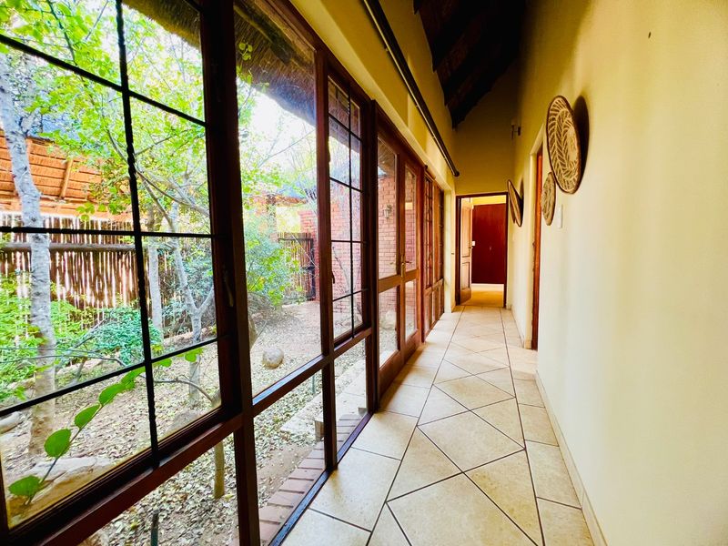 A bright, tiled hallway featuring extensive timber-framed glass doors that provide views of the garden and a high, exposed thatched roof.