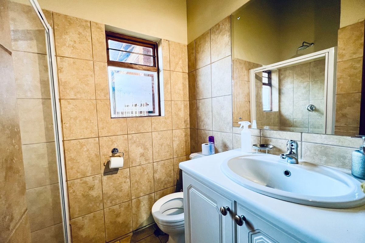 A functional bathroom featuring a vanity cabinet with a basin, a shower enclosure, and neutral wall tiling.