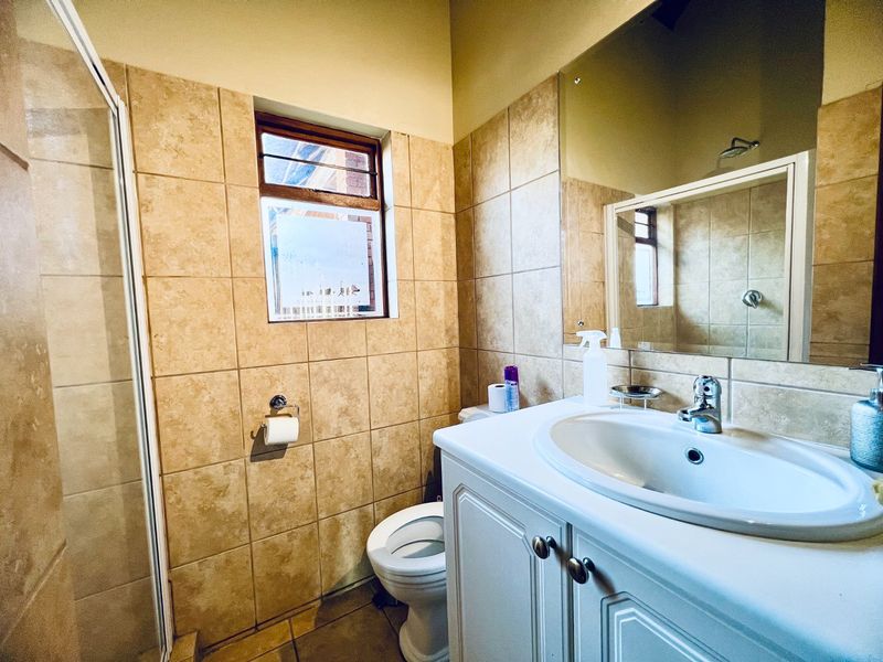 A functional bathroom featuring a vanity cabinet with a basin, a shower enclosure, and neutral wall tiling.
