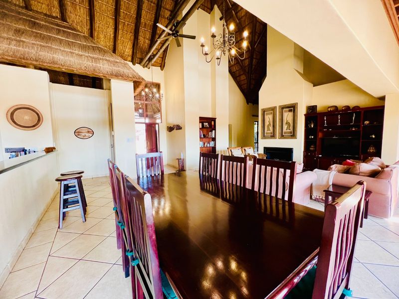 Spacious open-plan living and dining area featuring a high thatched ceiling with exposed trusses, a fireplace, and tiled flooring.