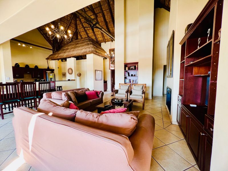 Spacious open-plan living area featuring a high thatched ceiling with exposed trusses, ceramic tiled flooring, a fireplace, and an integrated kitchen space.