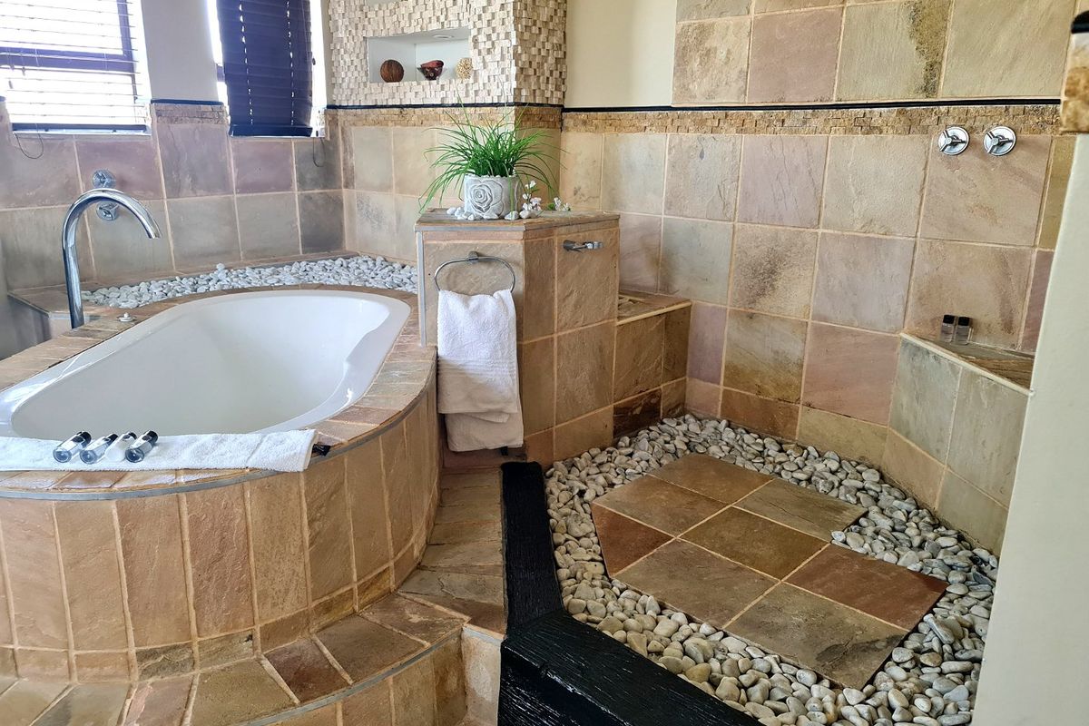 A spacious hotel bathroom featuring a built-in soaking tub, stone-tiled walk-in shower area with pebble flooring, and integrated wall niches.
