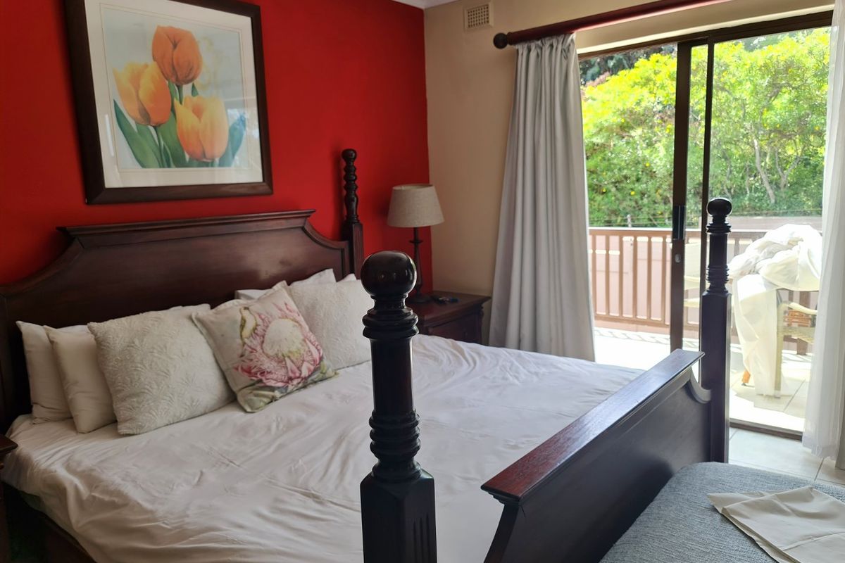 A bedroom featuring a red accent wall, sliding glass doors leading to a private balcony, and neutral flooring.