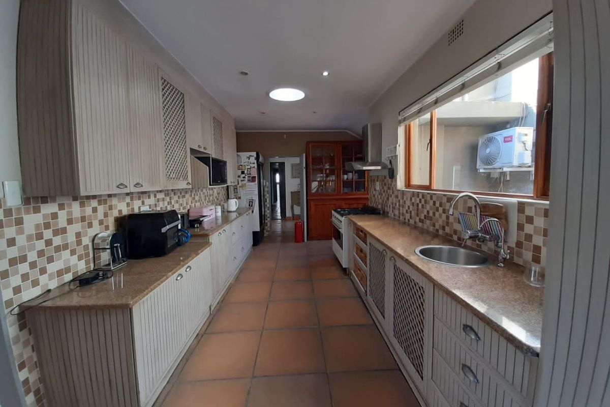 A galley-style kitchen featuring granite countertops, tiled backsplash, built-in cabinetry, and a stainless steel sink with a view to the exterior.