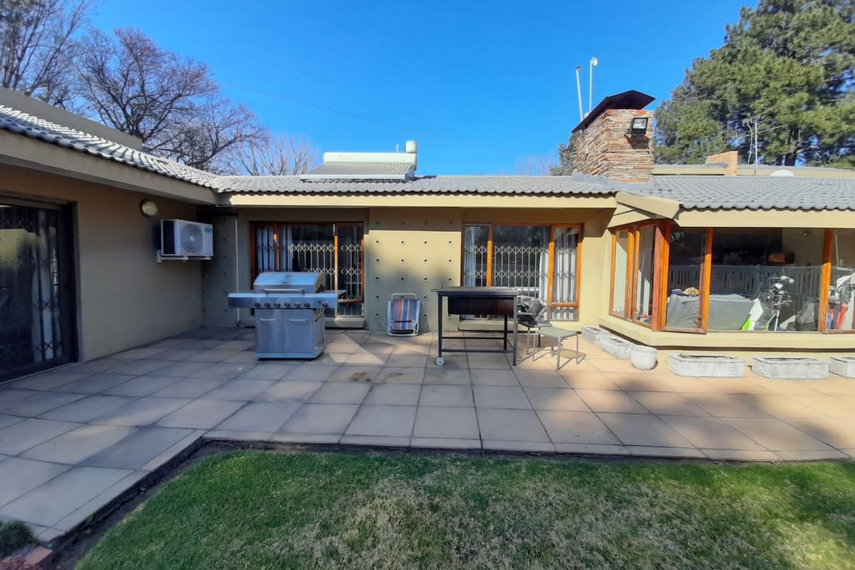 Spacious rear patio area featuring tiled flooring, stone chimney, and direct access to the garden through large glass sliding doors.