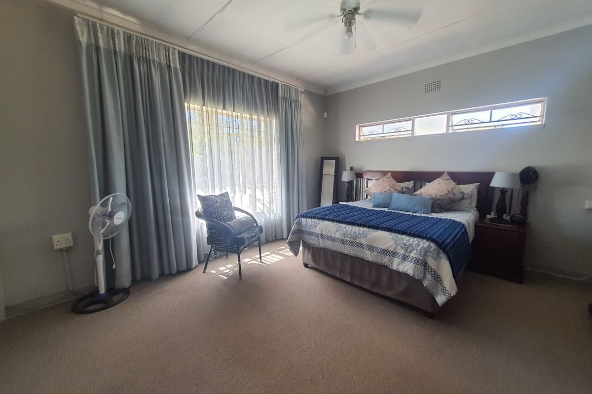 Spacious bedroom featuring neutral carpeting, a ceiling fan, and large windows with curtains providing ample natural light.