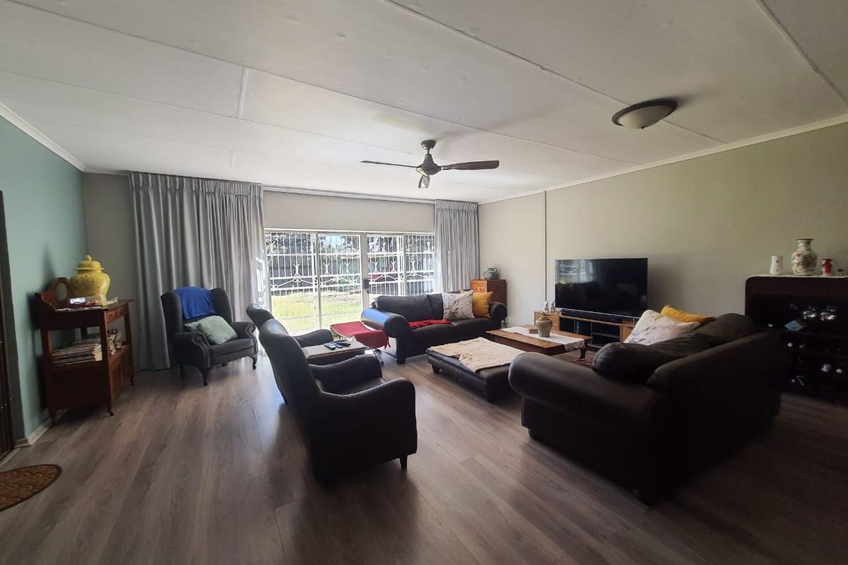 Spacious living room featuring wood-look laminate flooring, a ceiling fan, and large sliding glass doors with security gates leading to the exterior.