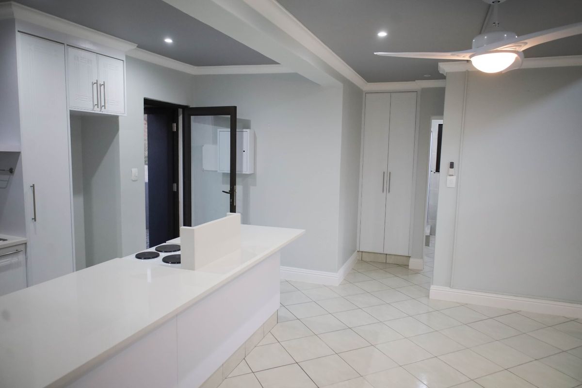 A modern, clean kitchen featuring white cabinetry, stone countertops with an integrated hob, tiled flooring, and recessed ceiling lighting.