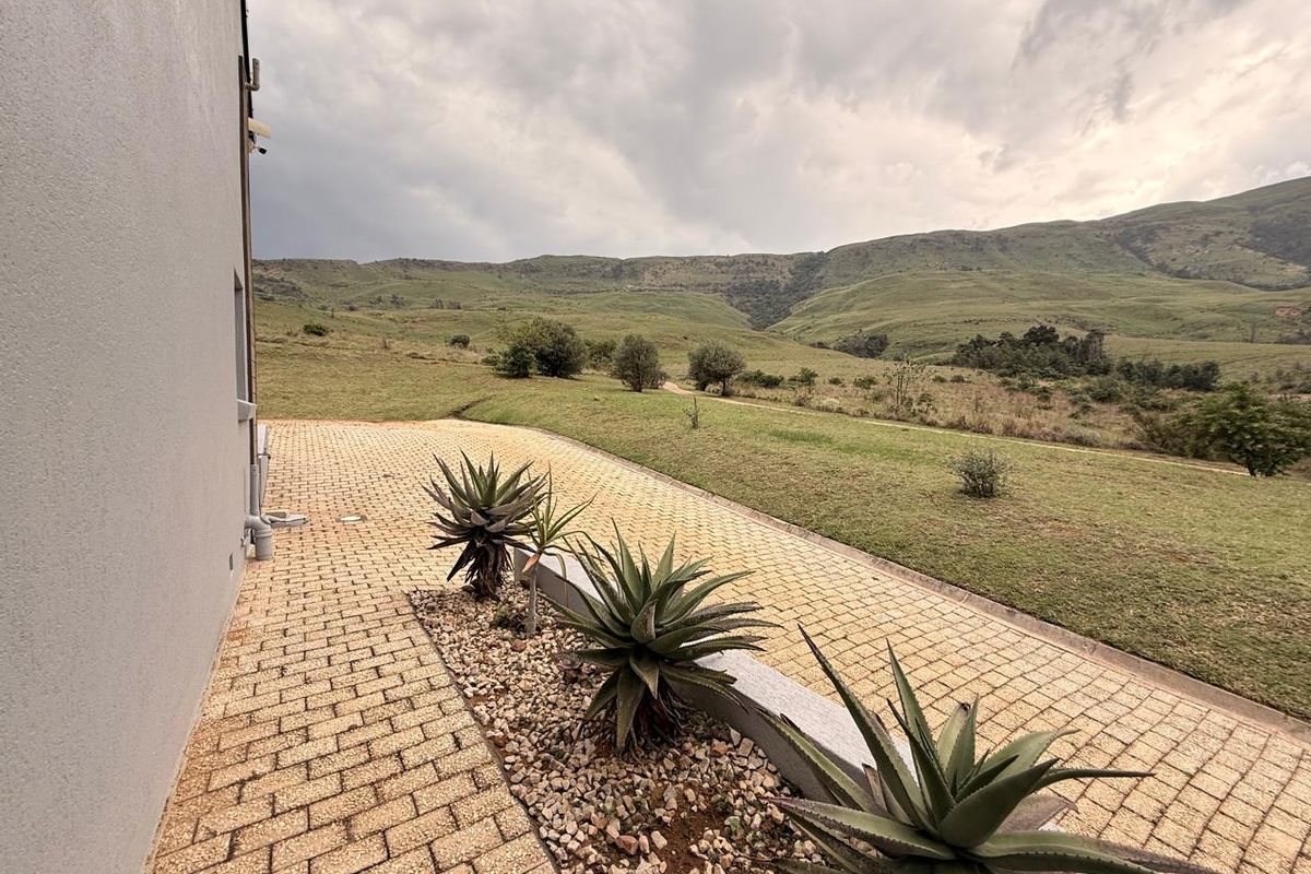 A paved rear walkway featuring a landscaped garden bed with succulents, overlooking expansive rolling hills and natural landscape.