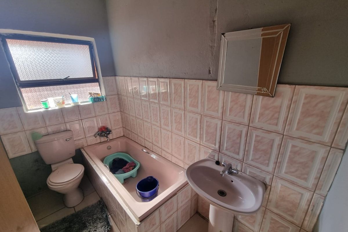 A dated bathroom featuring a pink bathtub, matching pedestal basin, and toilet, with tiled walls and a frosted glass window.