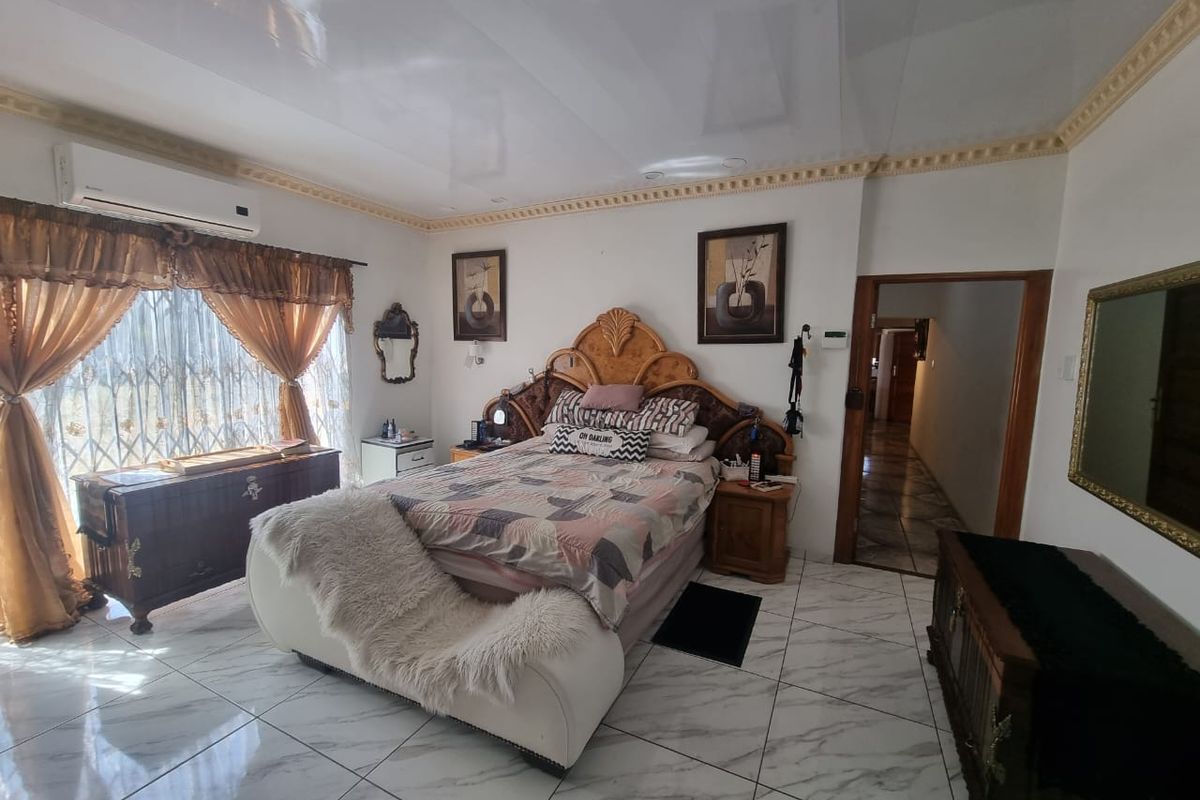 Spacious bedroom featuring glossy marble-look floor tiles, a wall-mounted air conditioning unit, and decorative crown molding.