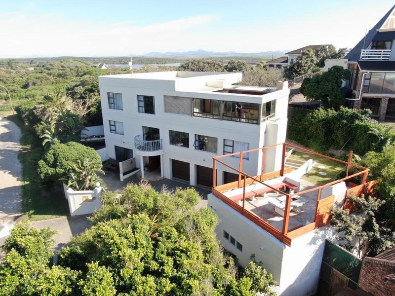 Aerial view of a multi-level residential property featuring a rooftop terrace, multiple garages, and a balcony, set within a landscaped coastal environment.