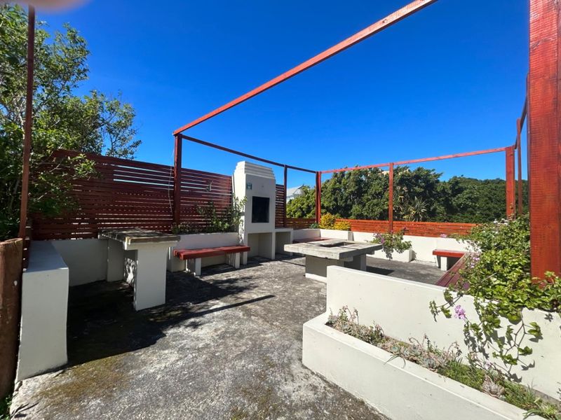 Outdoor patio area featuring a built-in braai, concrete seating, and timber pergola structure, ideal for alfresco dining and entertaining.