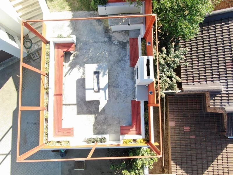 Aerial view of an outdoor entertainment area featuring a built-in fireplace, concrete fire pit, and integrated timber bench seating.