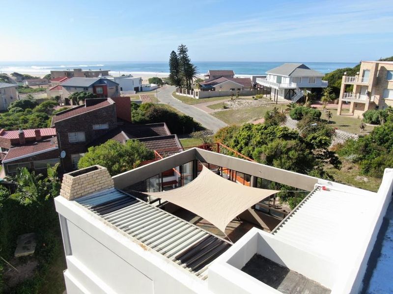 Elevated aerial view of a coastal property featuring a rooftop terrace with a shade sail, brick chimney, and expansive ocean views.