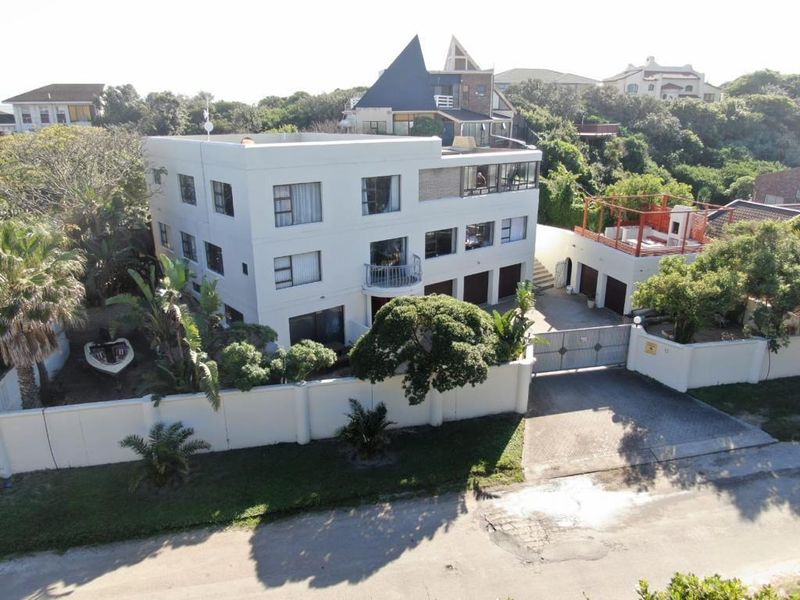 Aerial view of a multi-story residential property featuring a white facade, multiple garage bays, a gated driveway, and a rooftop terrace area.