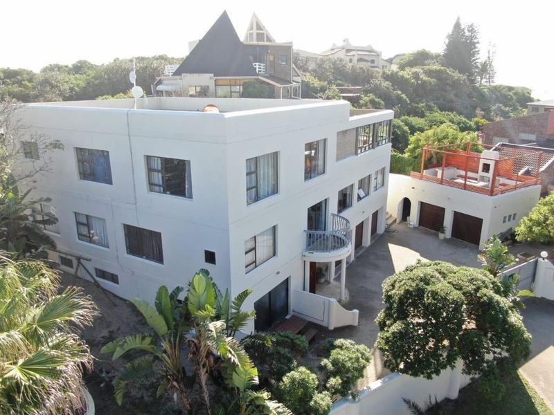 Aerial view of a multi-story residential property featuring a white facade, balcony, paved driveway, and a detached garage with a rooftop terrace.
