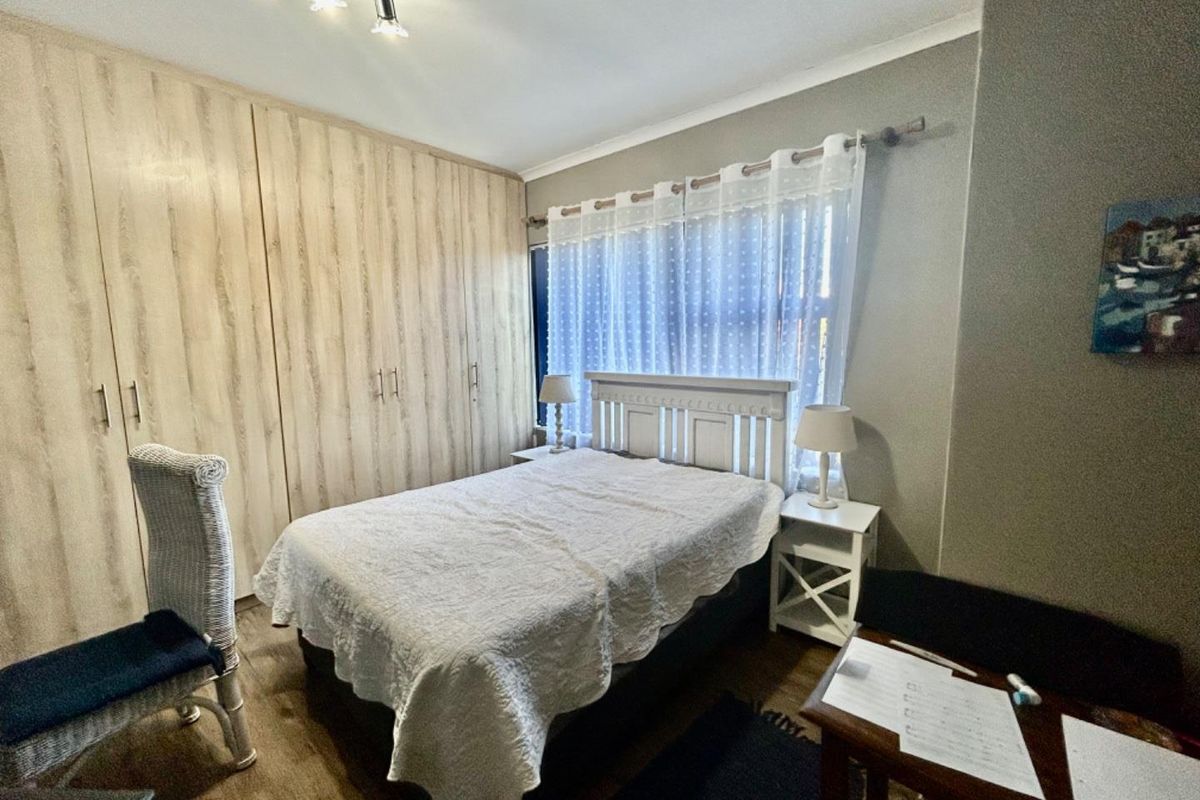 A well-maintained bedroom featuring light wood-grain built-in cupboards, laminate flooring, and modern track lighting.