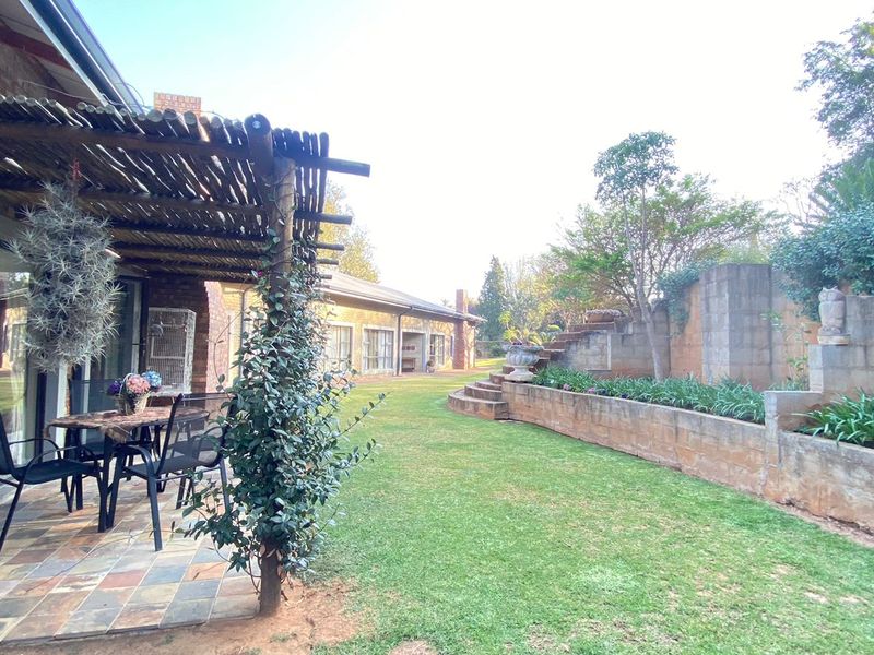 Rear garden view featuring a covered patio with a thatched pergola, slate flooring, and tiered brick retaining walls with established landscaping.