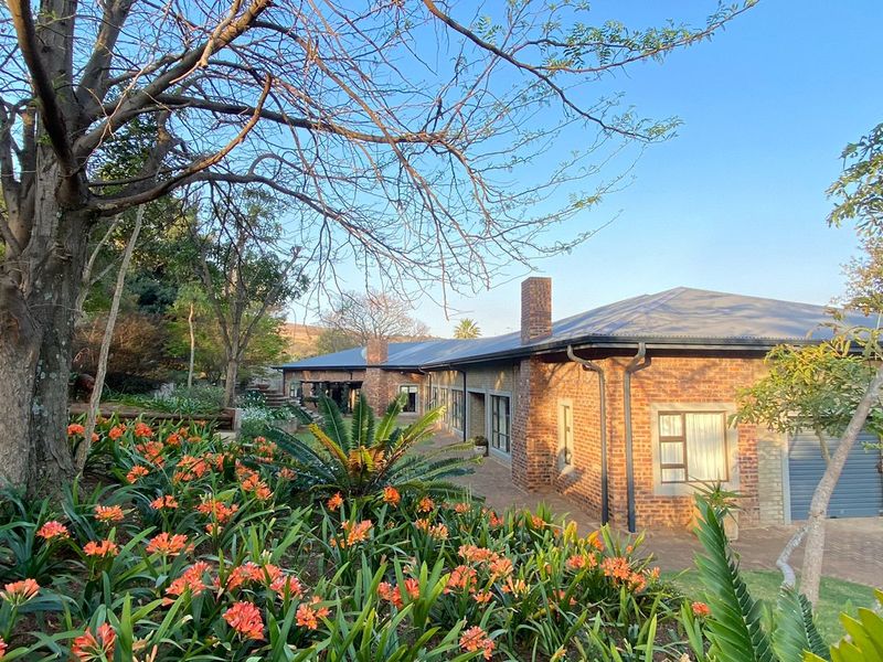 A well-maintained single-story face brick home featuring a pitched roof, brick chimney, and a beautifully landscaped garden with a paved driveway and garage access.