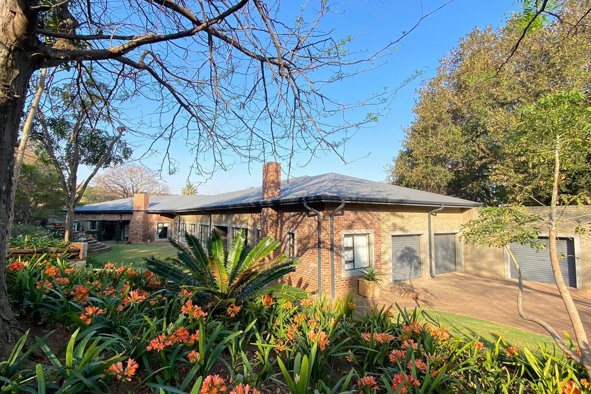 A well-maintained single-story brick house featuring a metal roof, double garage, and a spacious, landscaped garden with mature trees.