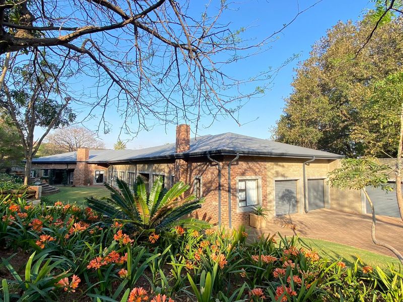 A well-maintained single-story brick house featuring a metal roof, double garage, and a spacious, landscaped garden with mature trees.