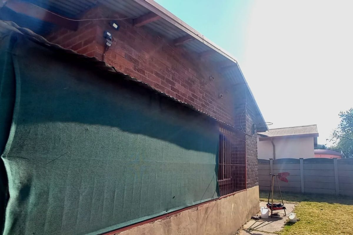 Rear exterior view of the house featuring exposed brick walls, corrugated roofing, and a shaded patio area overlooking the backyard.